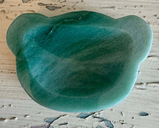 Green bear-shaped gua sha tool on textured white surface.