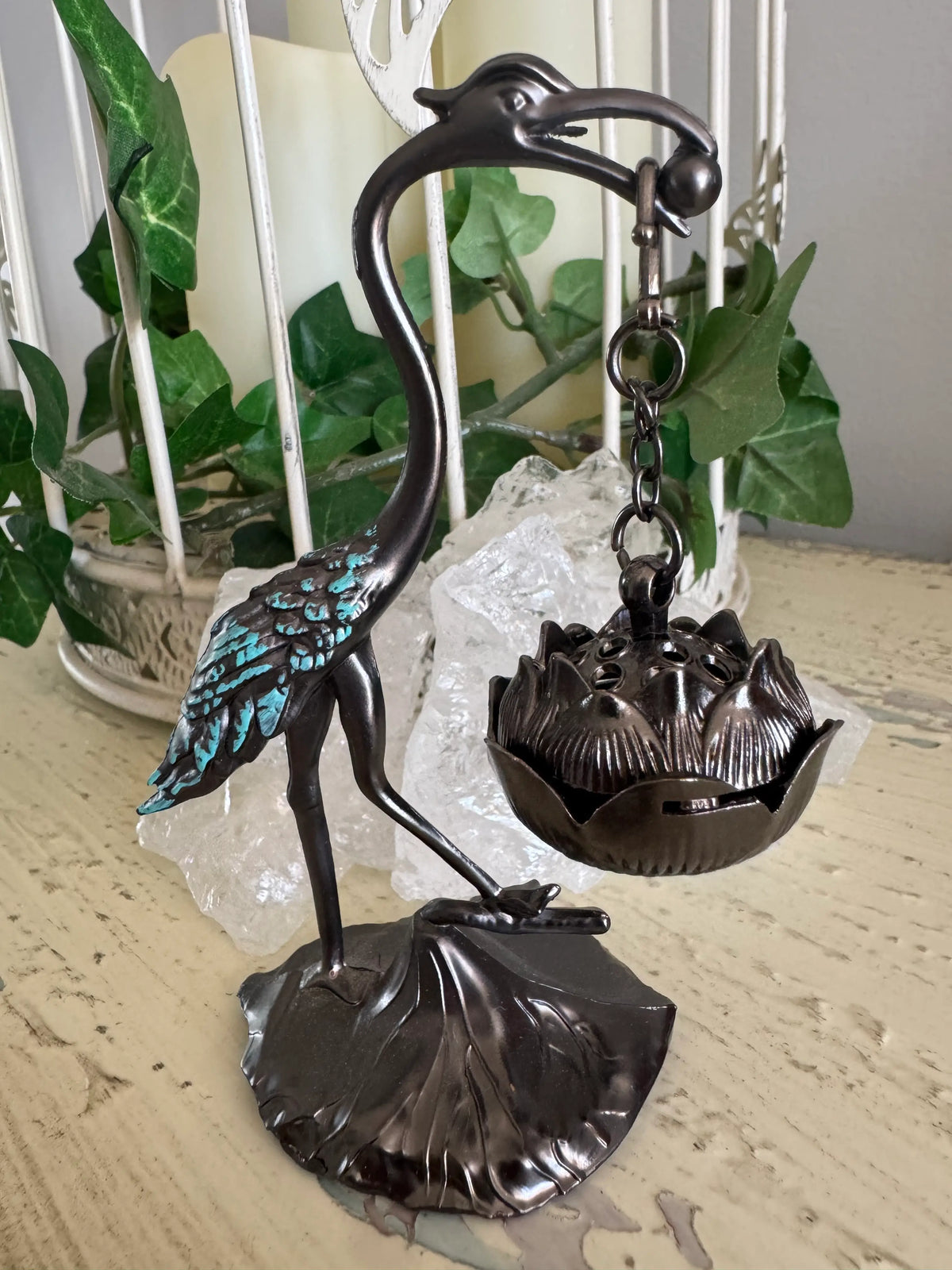 Bronze-colored crane incense burner, lotus-shaped pot, white quartz crystals, decorative cage, and faux ivy.
