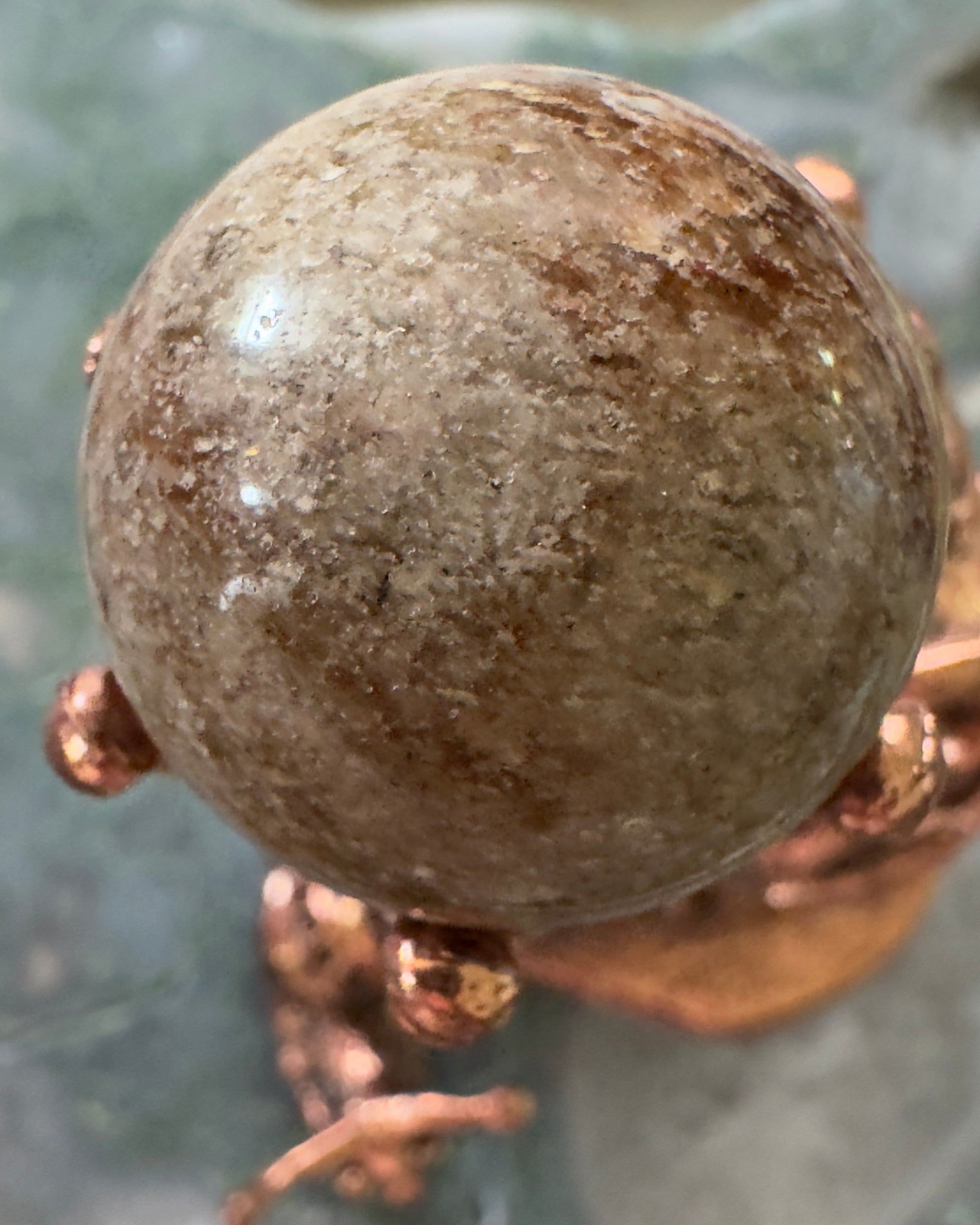 Brown speckled stone sphere on copper-colored metal stand.