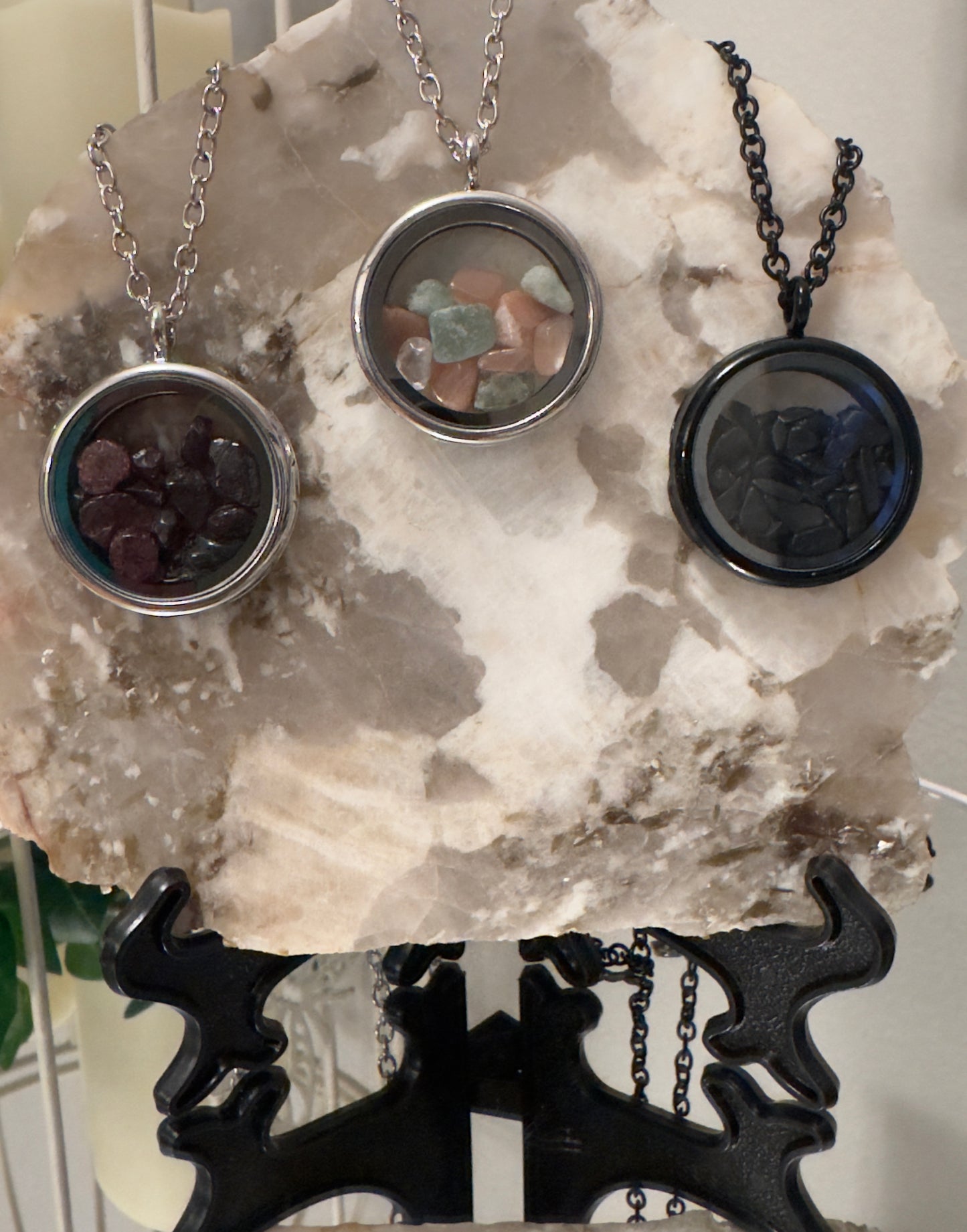 Three gemstone necklaces on a marble slab supported by a black metal stand.