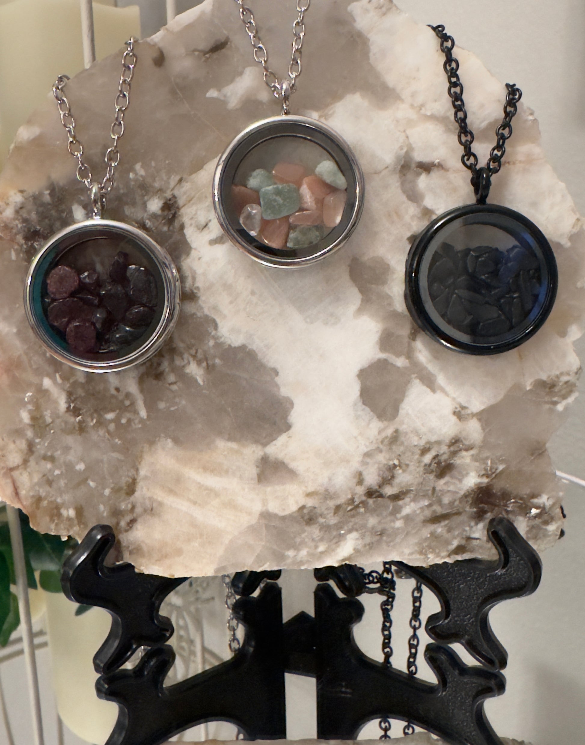 Three gemstone necklaces on a marble slab supported by a black metal stand.