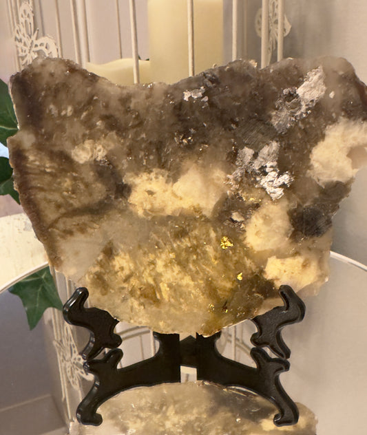 Stone art piece with gold and silver embellishments on a black display stand.