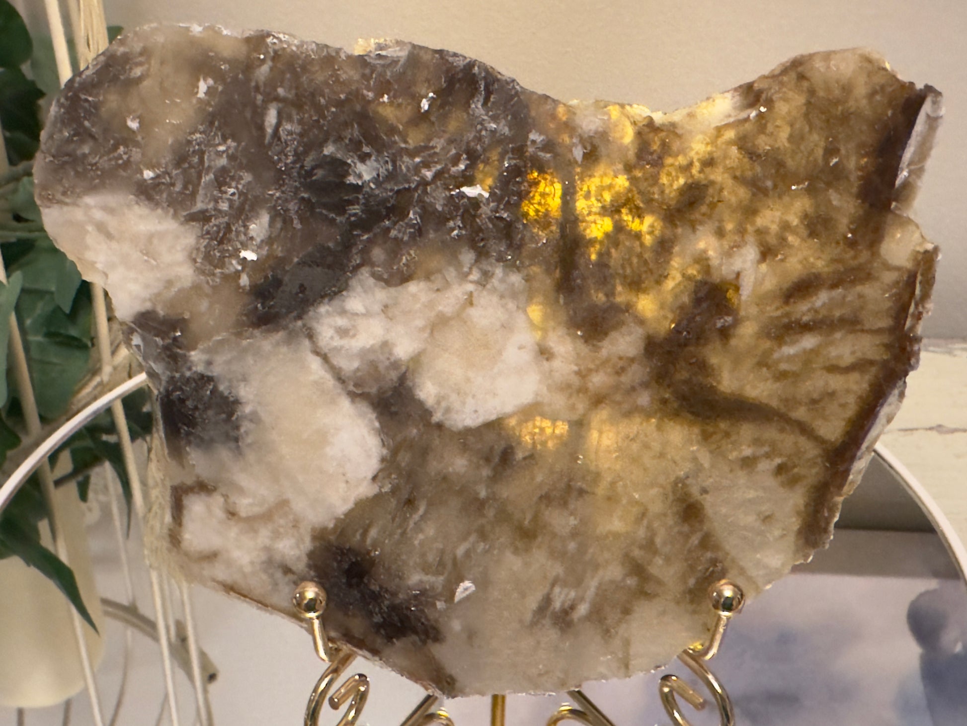 Polished slab of translucent agate in beige and brown hues on gold stand.
