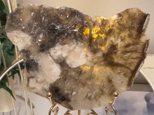 Polished slab of translucent agate in beige and brown hues on gold stand.
