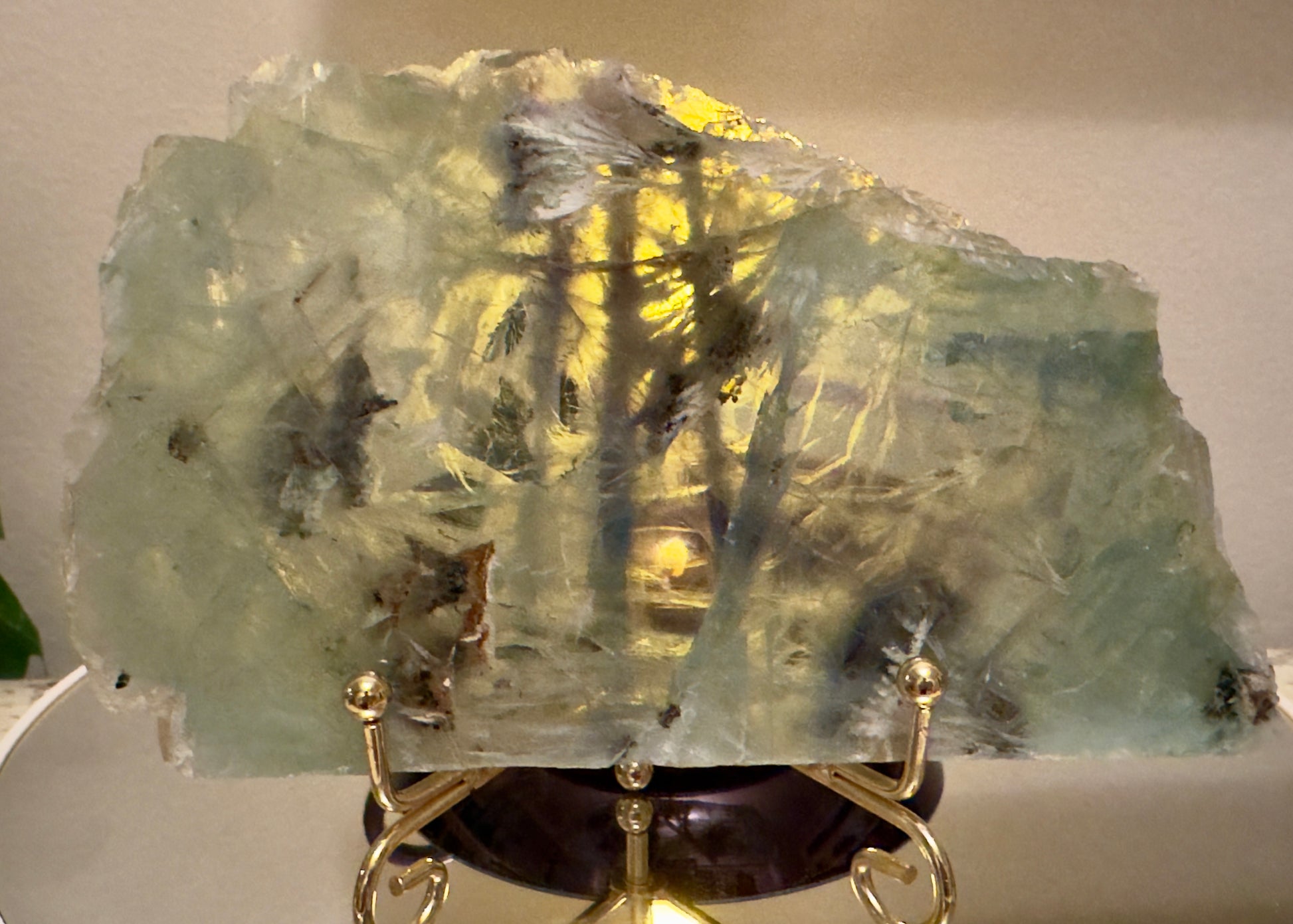 Large, light-green and yellow crystal slice on gold stand.
