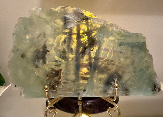 Large, light-green and yellow crystal slice on gold stand.
