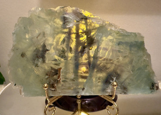 Large, light-green and yellow crystal slice on gold stand.
