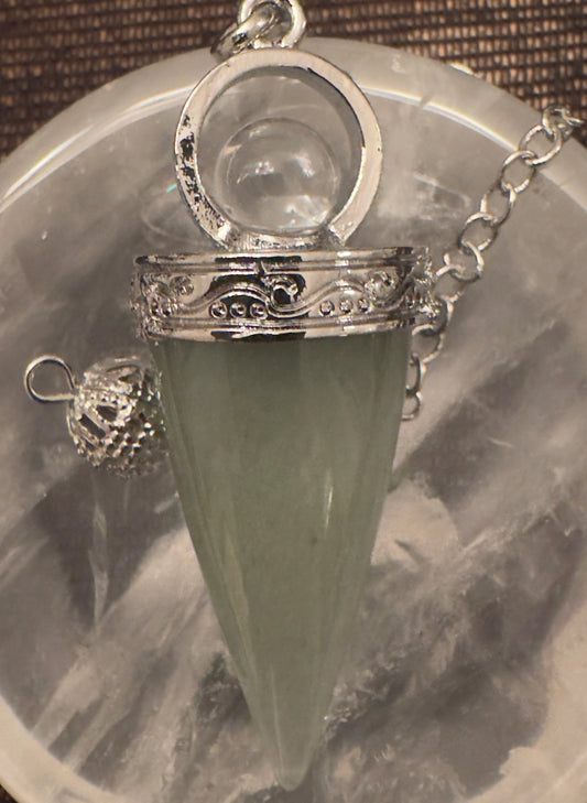 A green cone-shaped pendant with silver fittings and chain rests on a clear quartz sphere.