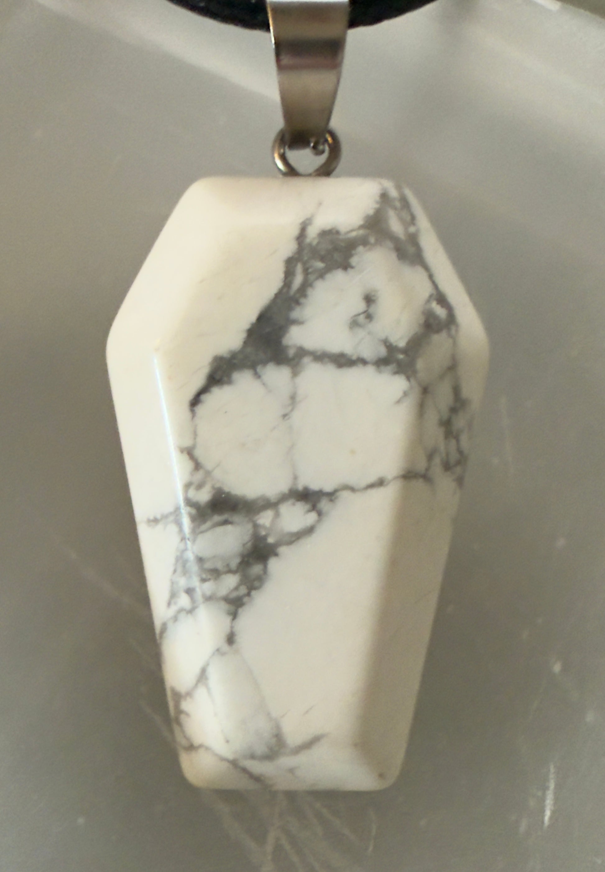 White marble pendant with silver bail and black cord.