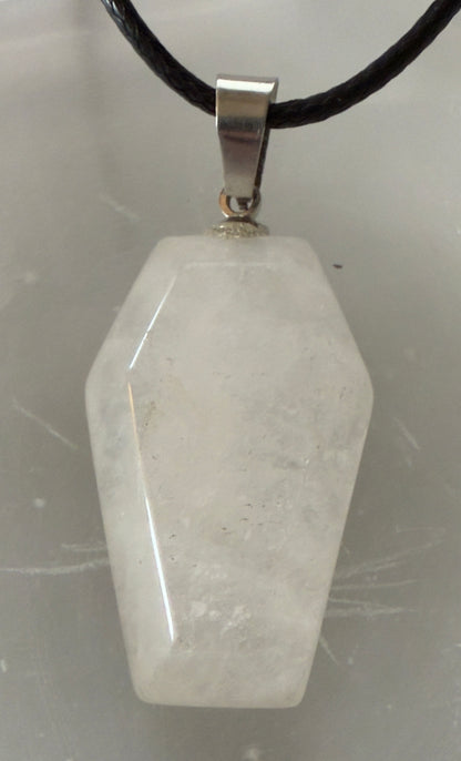A white coffin-shaped quartz crystal pendant with a silver bail hanging on a black braided cord.