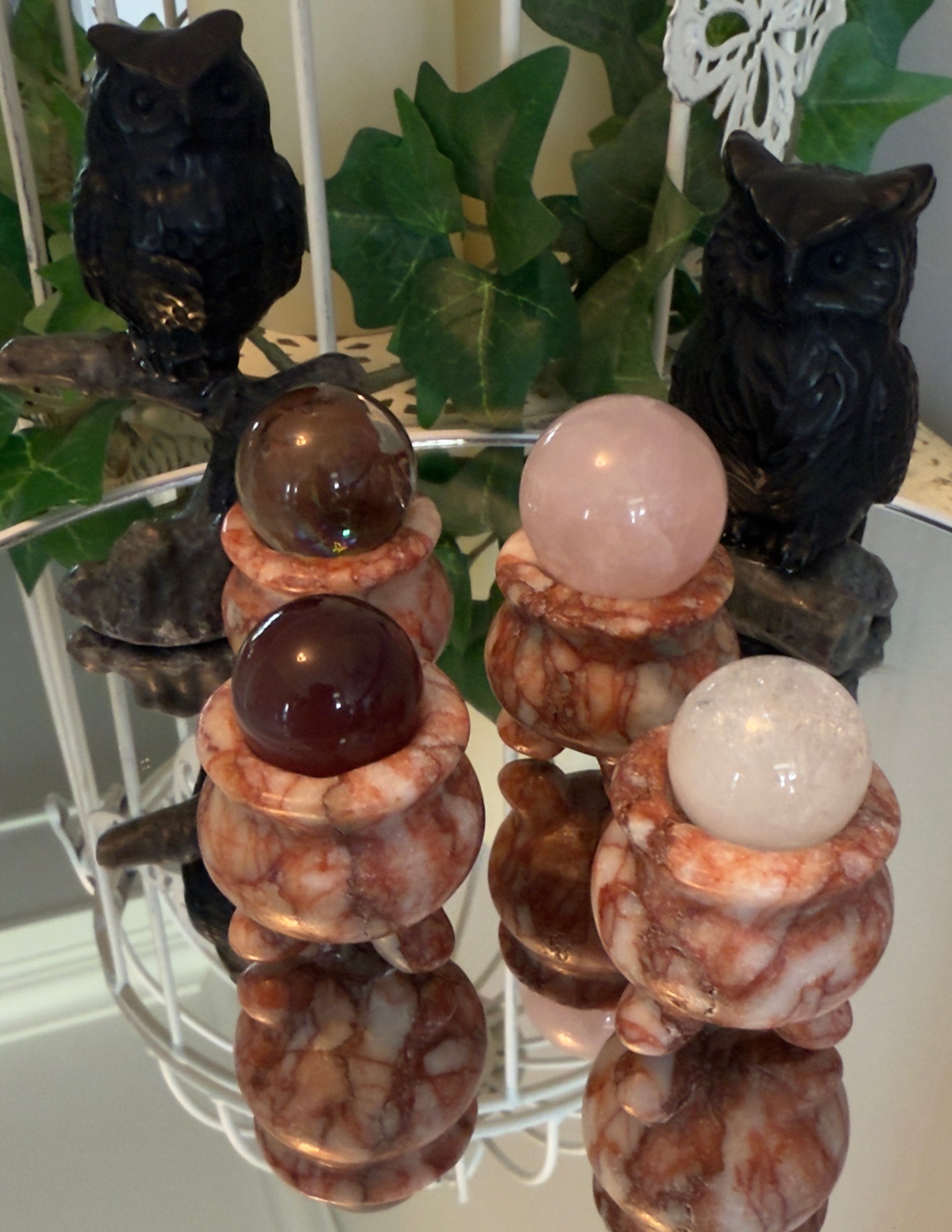 Four crystal spheres in marble holders with two owl figurines on a mirrored surface.