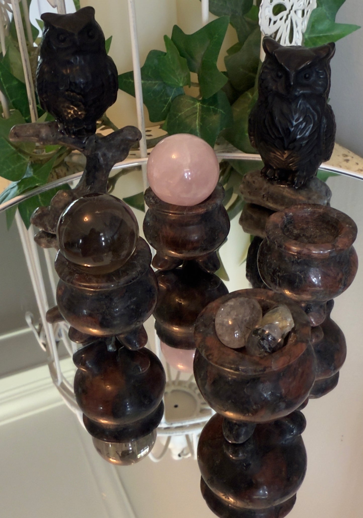 Two dark stone owls and three stacked crystal balls on decorative stands reflected in a mirror.