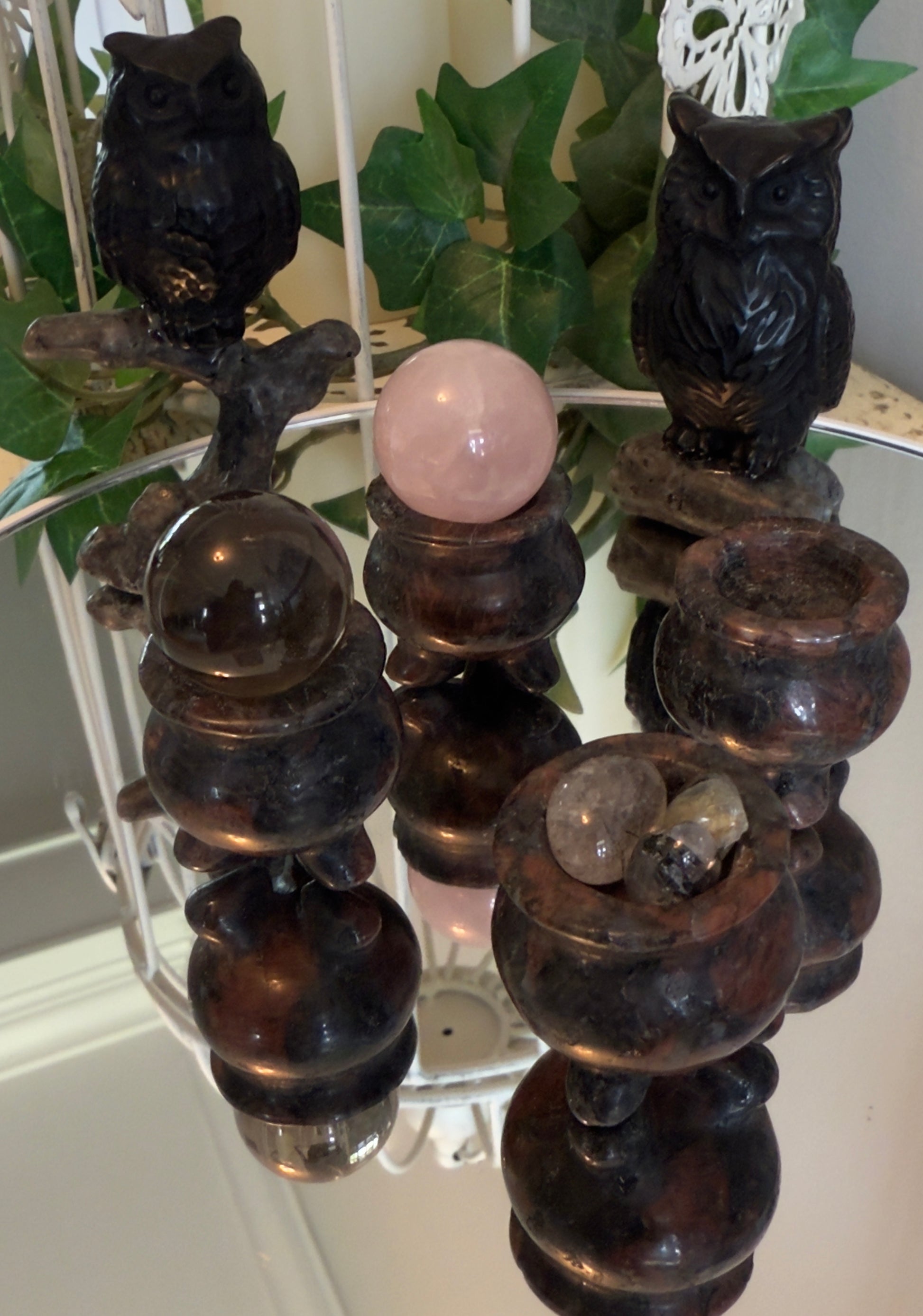Two dark stone owls and three stacked crystal balls on decorative stands reflected in a mirror.