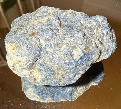 A rough, blue and white stone sits atop a reflective surface.