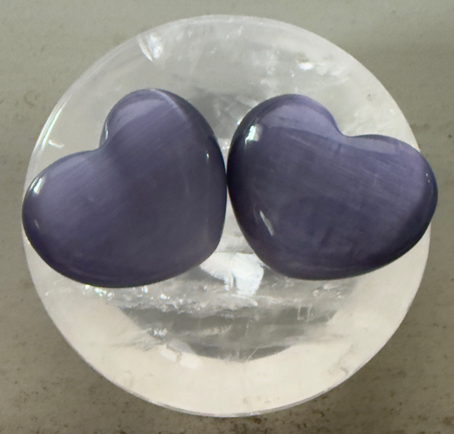 Two lavender heart-shaped stones on a round, clear surface.
