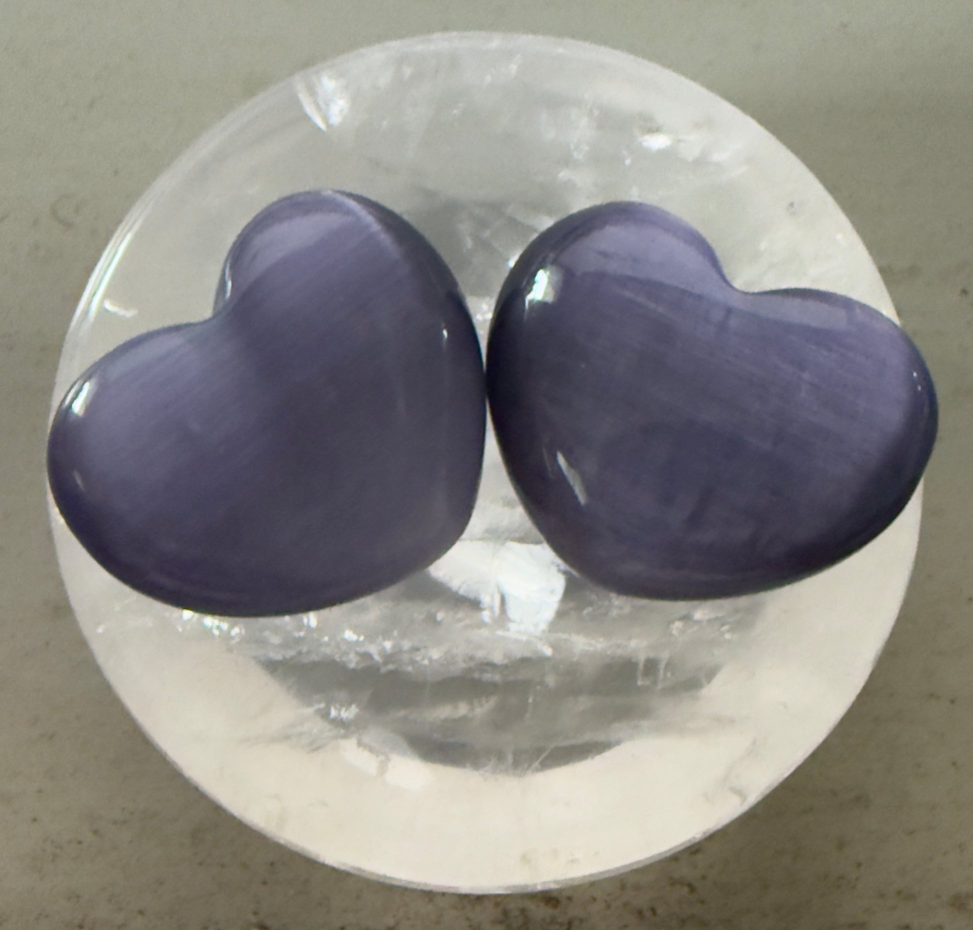 Two lavender heart-shaped stones on a round, clear surface.