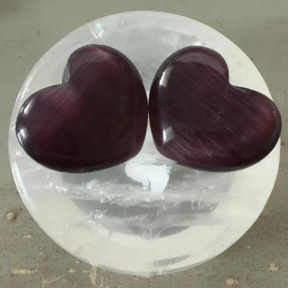 Two dark purple chatoyant selenite carved hearts in a clear quartz bowl 