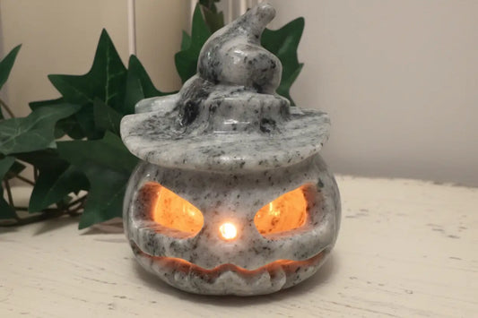 Jade carved jack o’lantern with candle light sitting on a table with green leaves behind