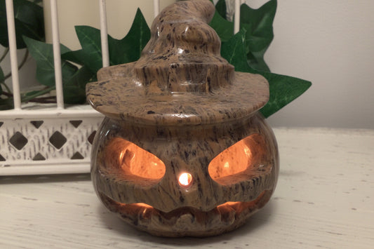  Dendritic Jasper Jack O’Lantern Carving sitting on a white table with greenery behind and candle light inside 