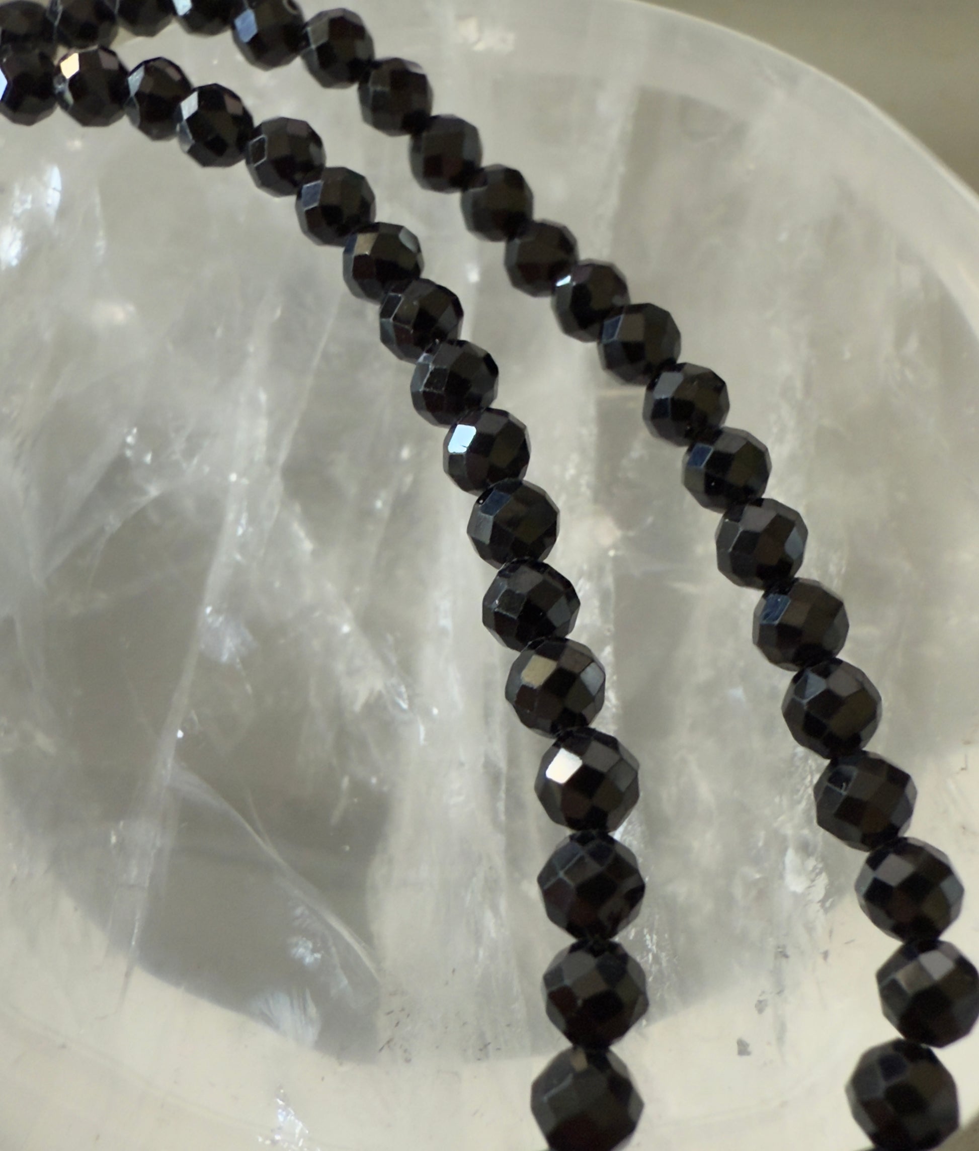 Two strands of faceted black beads lie against a translucent crystal bowl.
