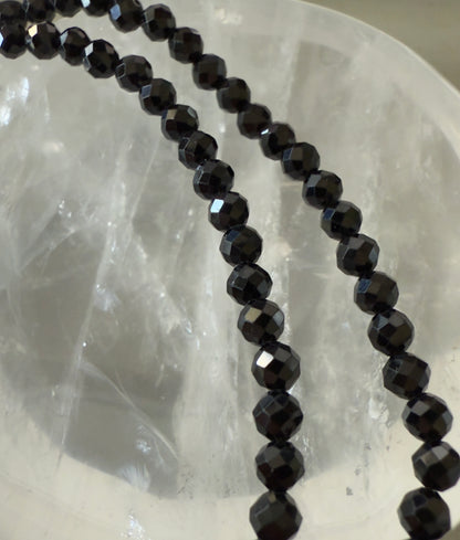 Two strands of faceted black beads lie against a translucent crystal bowl.