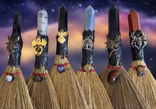 A row of handmade ritual brooms with crystal handles and decorative charms against a starry background.