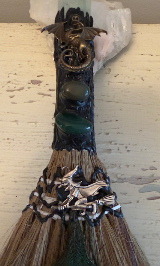 Close-up of a decorative witch's broom with dragons, stones, and a witch figure.