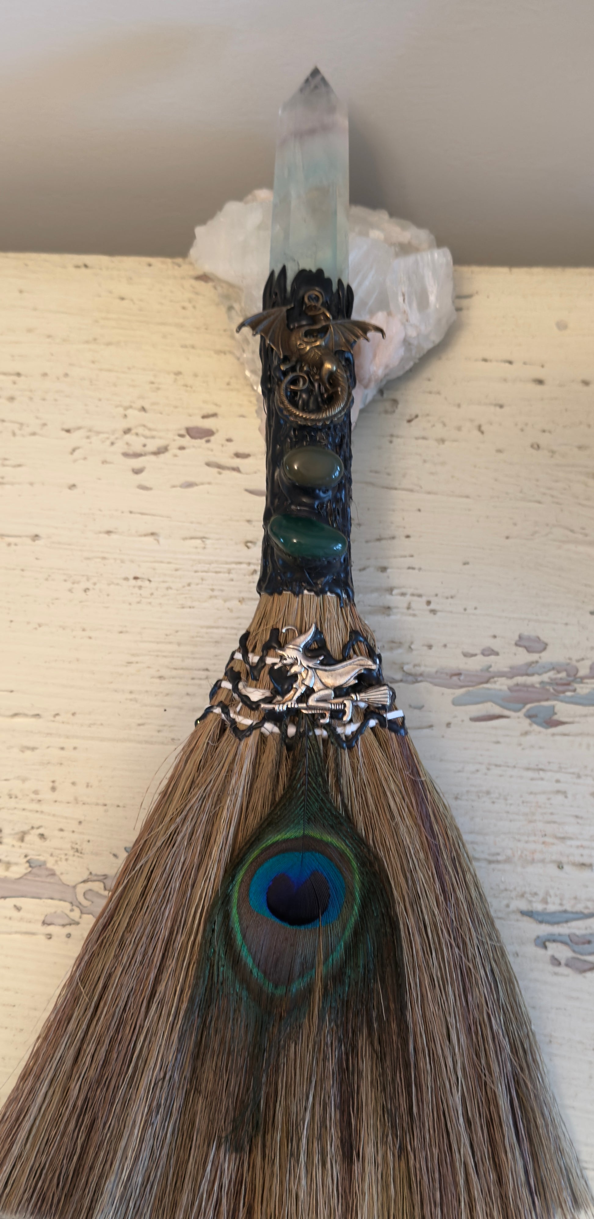 Witch's broom with dragon, crystals, and peacock feather.
