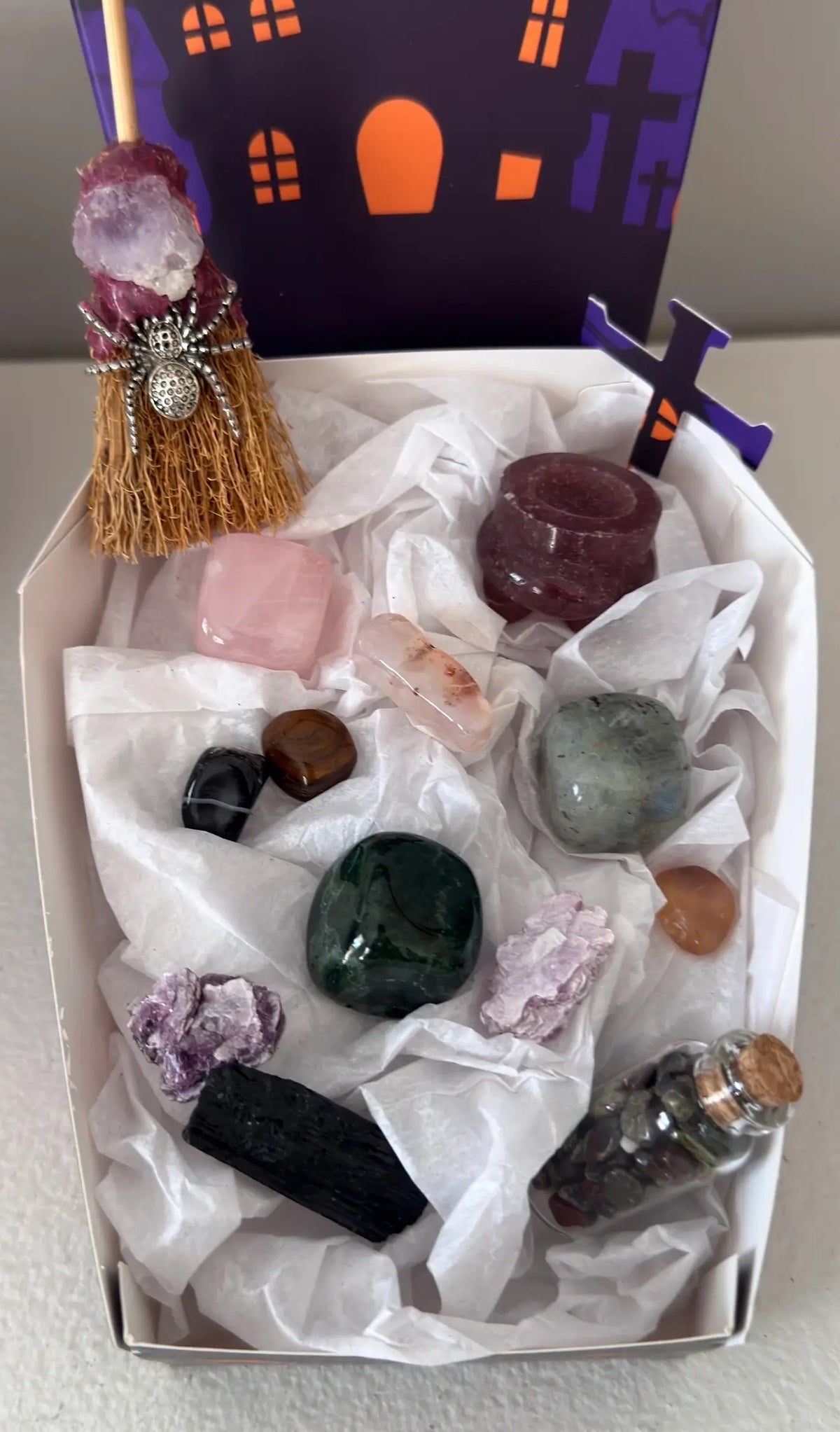 photo showing close up of all pieces in the bundle, strawberry quartz, rose quartz, green jasper, labradorite, black tourmaline, mica. Witches broom with amethyst and spider charm.  Assorted tumbles and wish bottle filled with dragon’s blood crystal chips