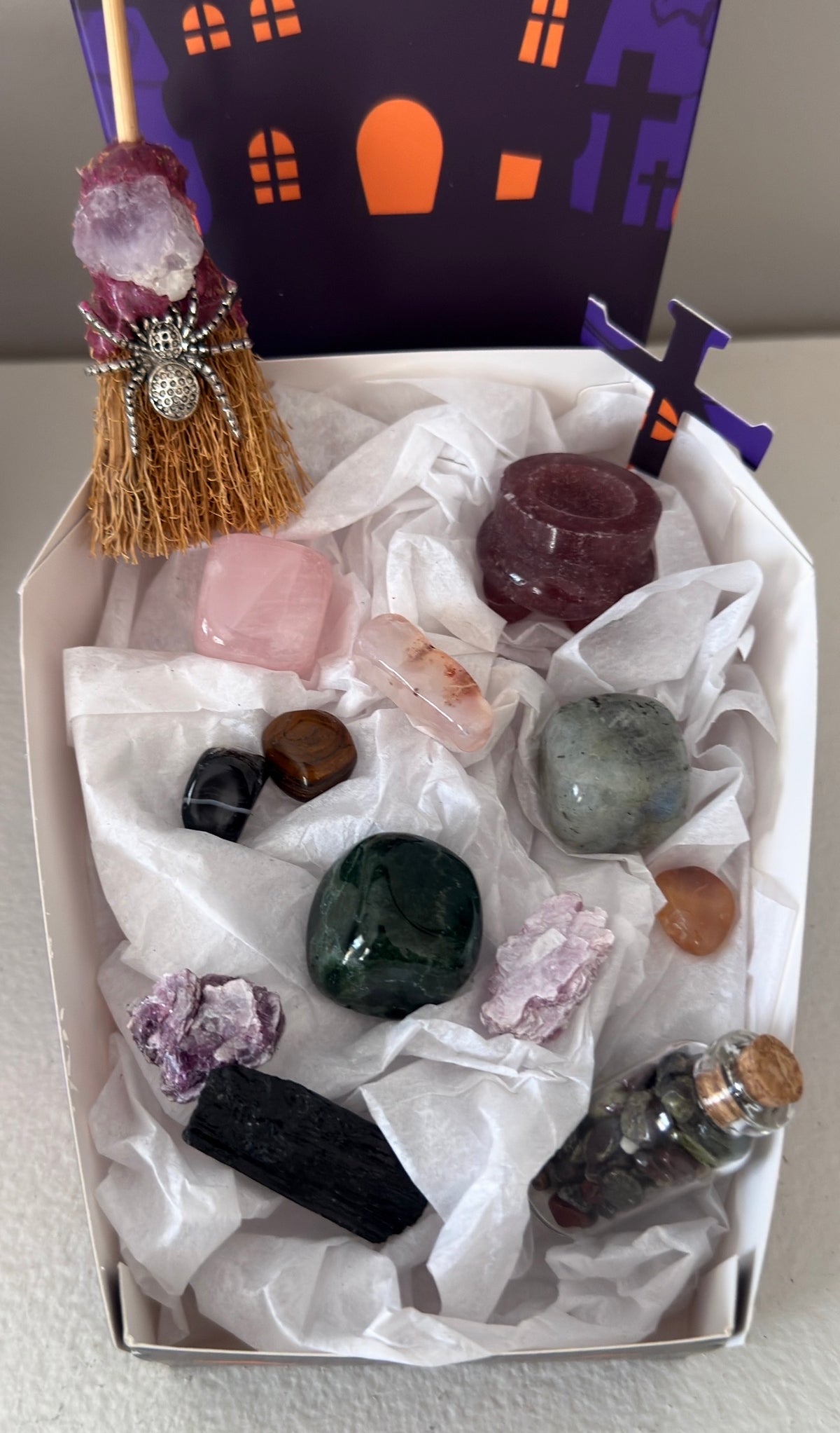photo showing close up of all pieces in the bundle, strawberry quartz, rose quartz, green jasper, labradorite, black tourmaline, mica. Witches broom with amethyst and spider charm.  Assorted tumbles and wish bottle filled with dragon’s blood crystal chips