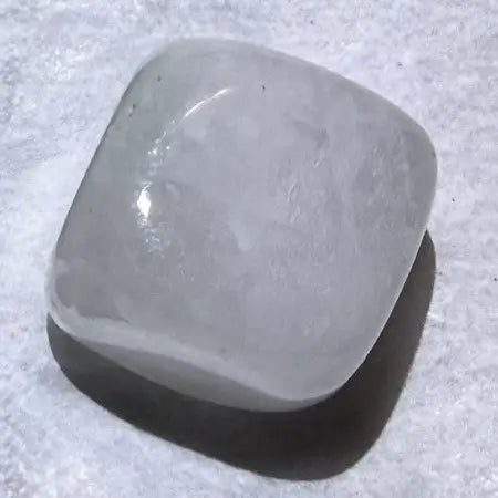 A polished, rounded square stone with a smooth, matte gray surface and a glossy highlight, resting on a textured light gray background with a soft shadow.