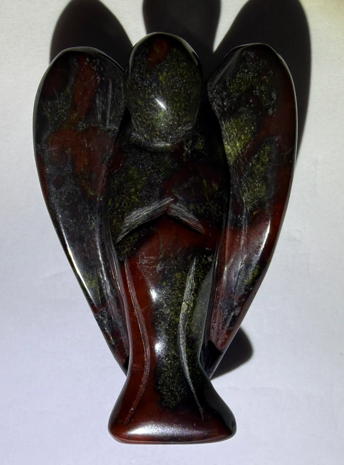 photo of natural dragon’s blood crystal carved angel. Details include wings and angels arms folded. 