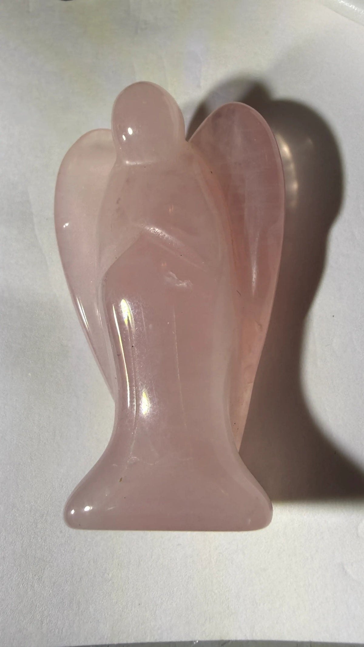photo of side of hand carved rose quartz angel.  angel has carving details like wings and folder arms 