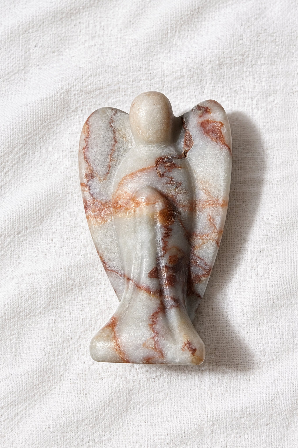 Red Vein Jasper carved angel with wings resting on a white background