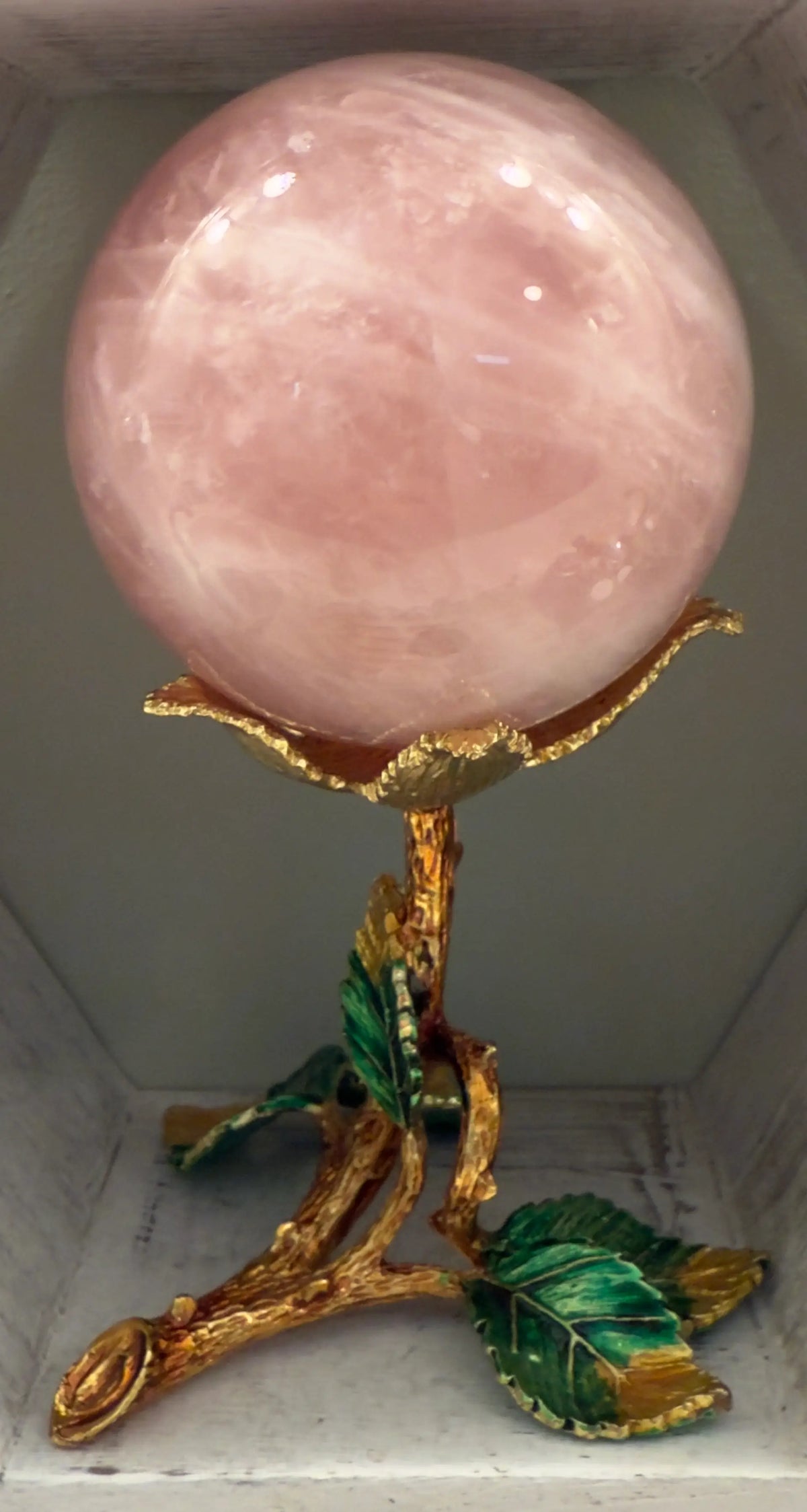 Close up of a Rose Quartz Sphere in a gold toned stand