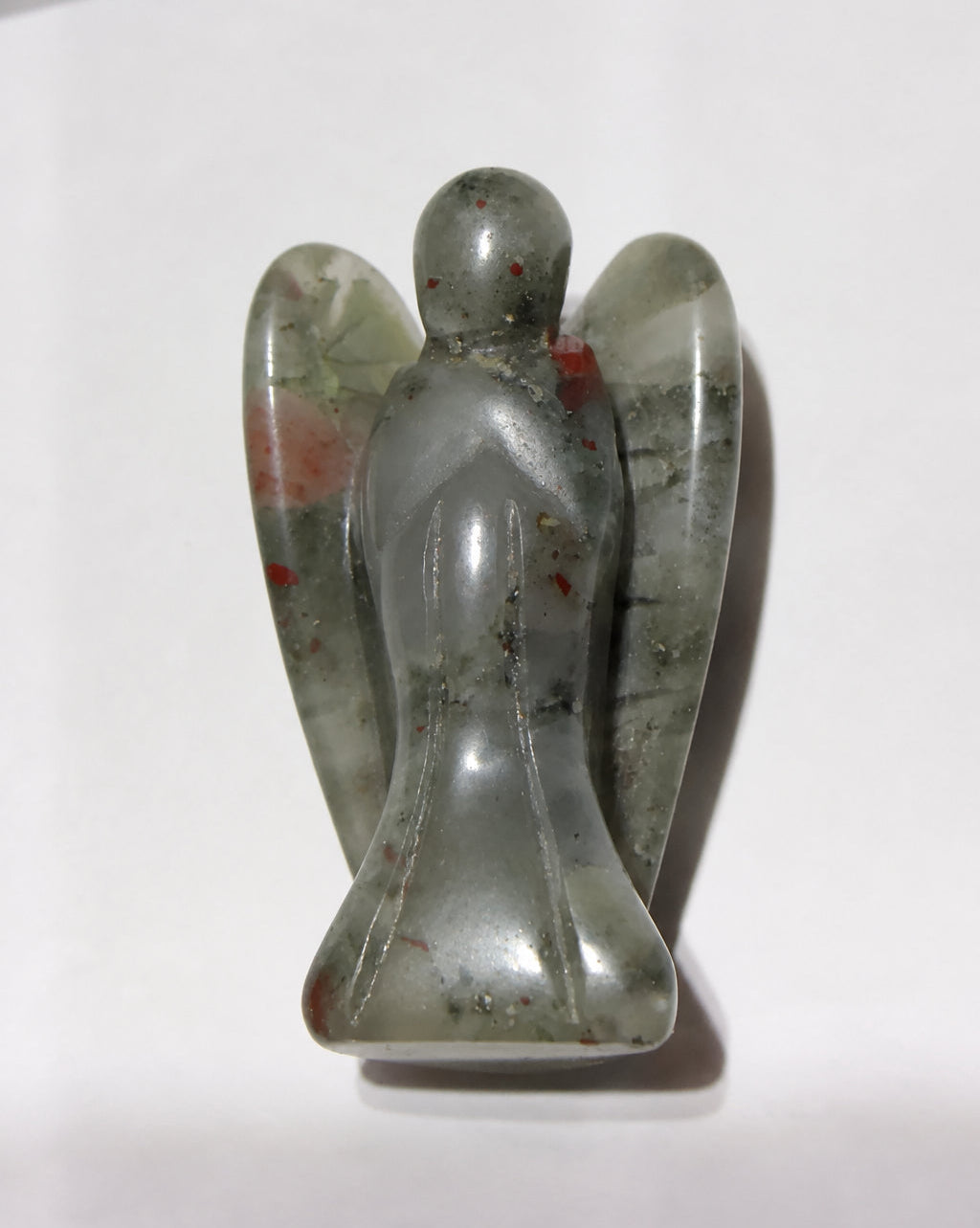 A small carved angel figurine made of bloodstone with natural red and green inclusions, standing on a plain white surface.