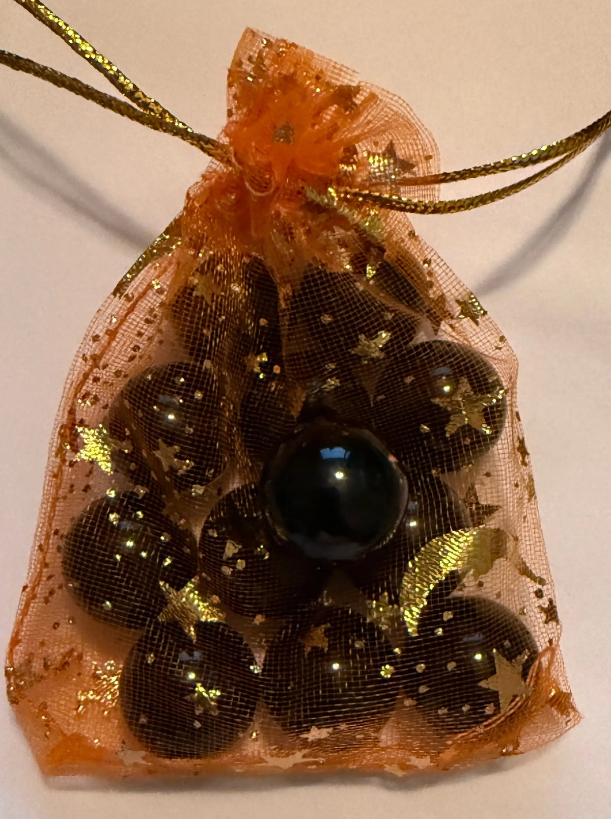 An orange sheer organza drawstring pouch decorated with gold glitter and star patterns, containing several black agate mini spheres.