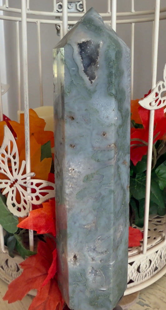 Natural Dark Green Moss Agate Tower with Druzy Pockets in front of a bird cage with autumn flowers behind