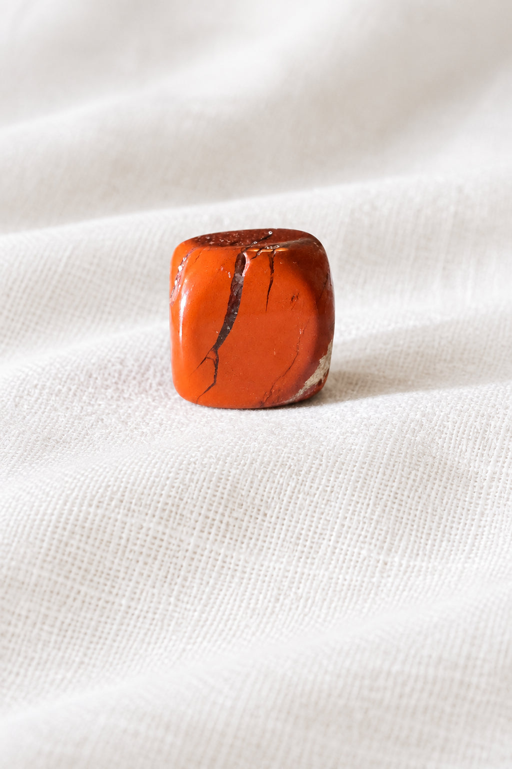 close up photo one brecciated jasper carved crystal cube on a white surface