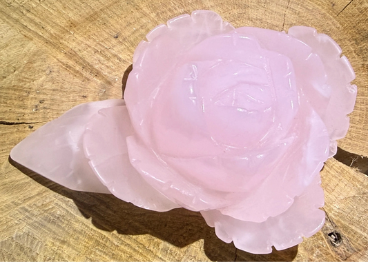 A carved pink rose quartz crystal  displayed on a rustic wood slice background.
