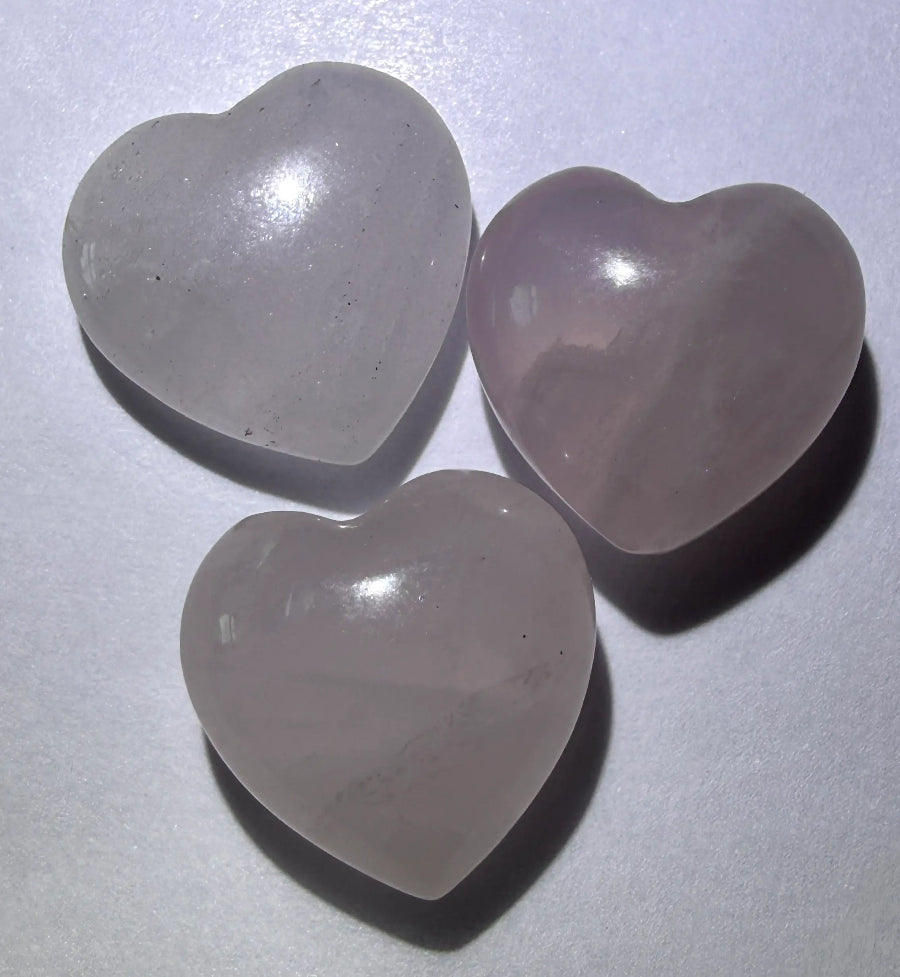 Three rose quartz mini carved hearts resting on a white background with dramatic drop shadows