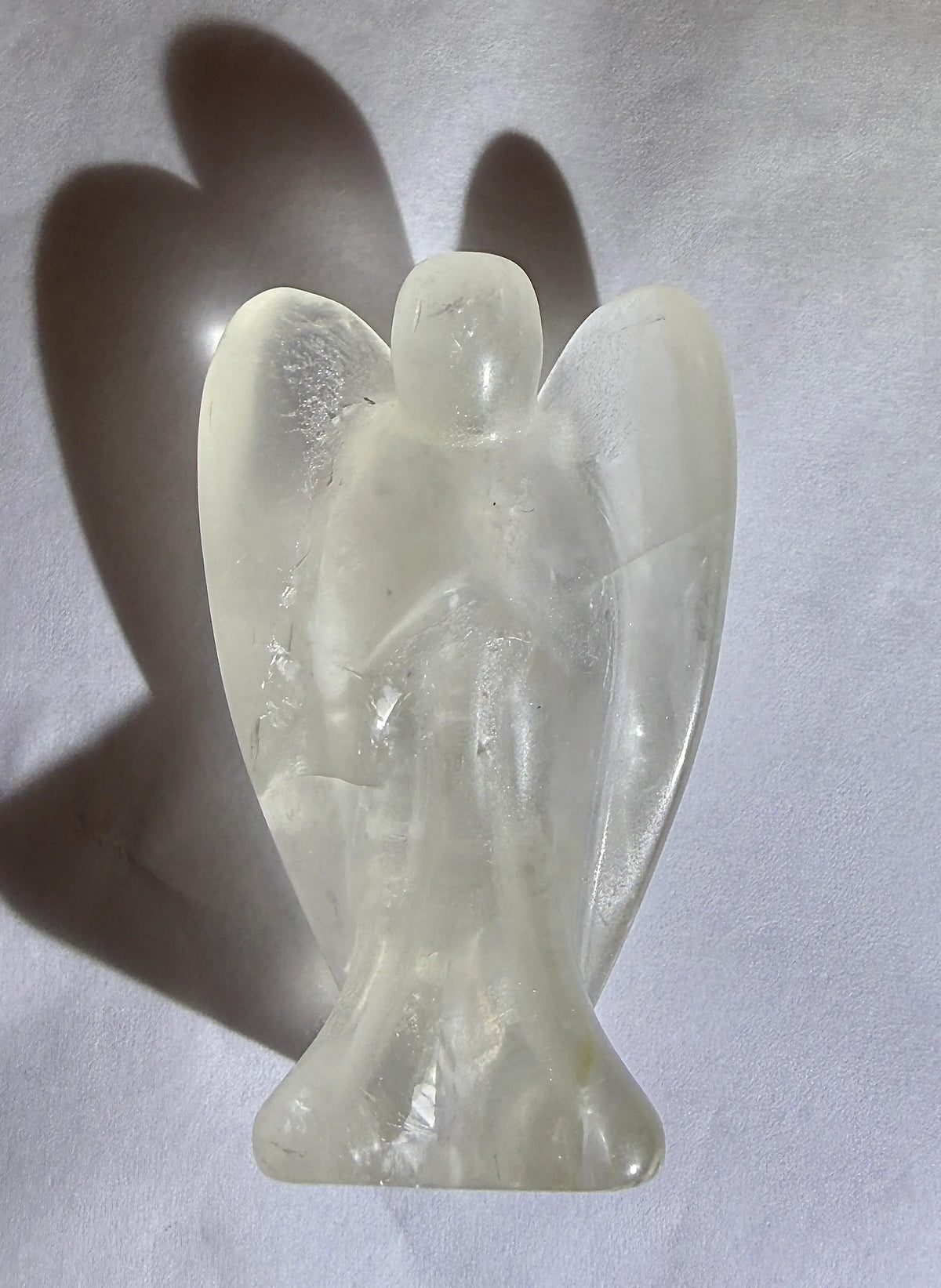 close up photo clear quartz hand carved angel resting on a white backround with a deep drop shadow.  Obvious Iron Oxide and rutile inclusions