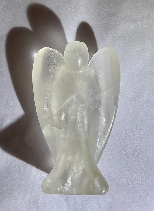 close up photo clear quartz hand carved angel resting on a white backround with a deep drop shadow.  Obvious Iron Oxide and rutile inclusions