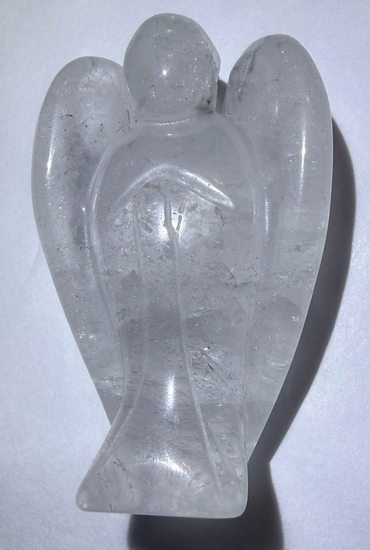 photo of hand carved clear quartz angel with wings and rutile inclusions resting on a white background