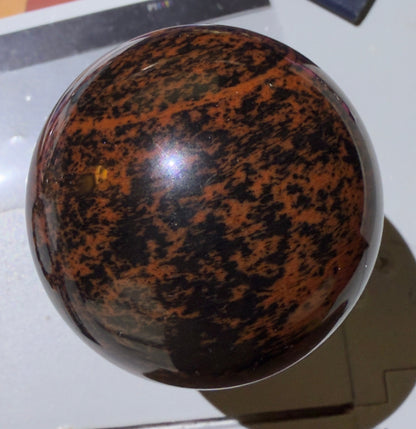 Polished mahogany obsidian sphere with deep chocolate brown and black patterns, natural gemstone crystal ball for metaphysical decor, grounding, and crystal healing from Mainstreet Crystals and Minerals.