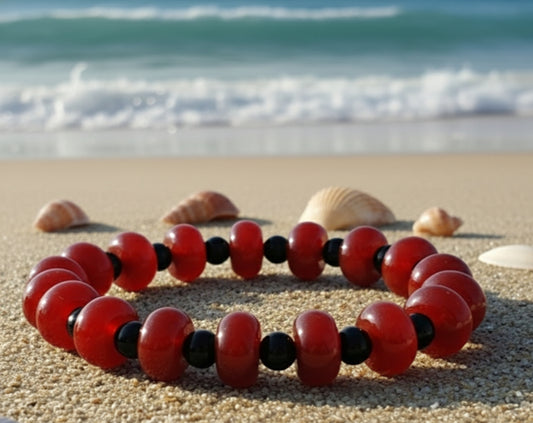 Carnelian and Black Obsidian Bracelet  Bright Reddish Orange with Black sphere shaped spacers  sitting on the sand with the ocean waves behind 