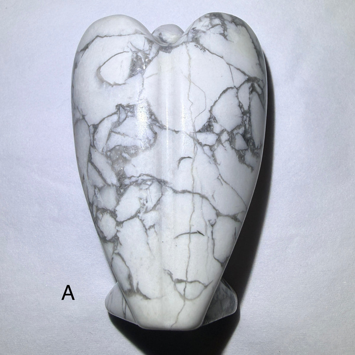 close up photo of angel, hand carved from howlite, resting on a white background Angel A