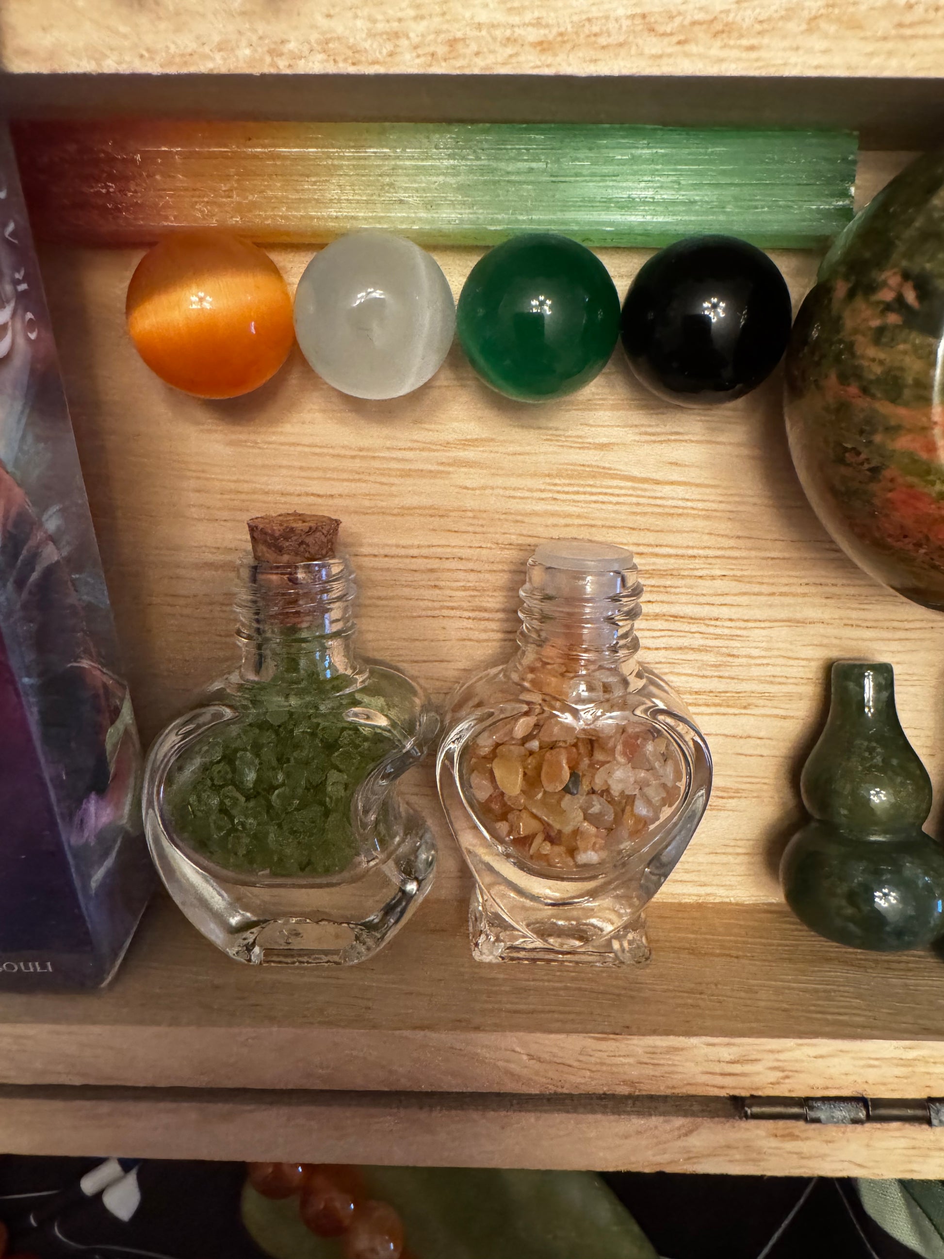 Wooden box filled with small glass bottles, round gemstones, and other decorative objects.