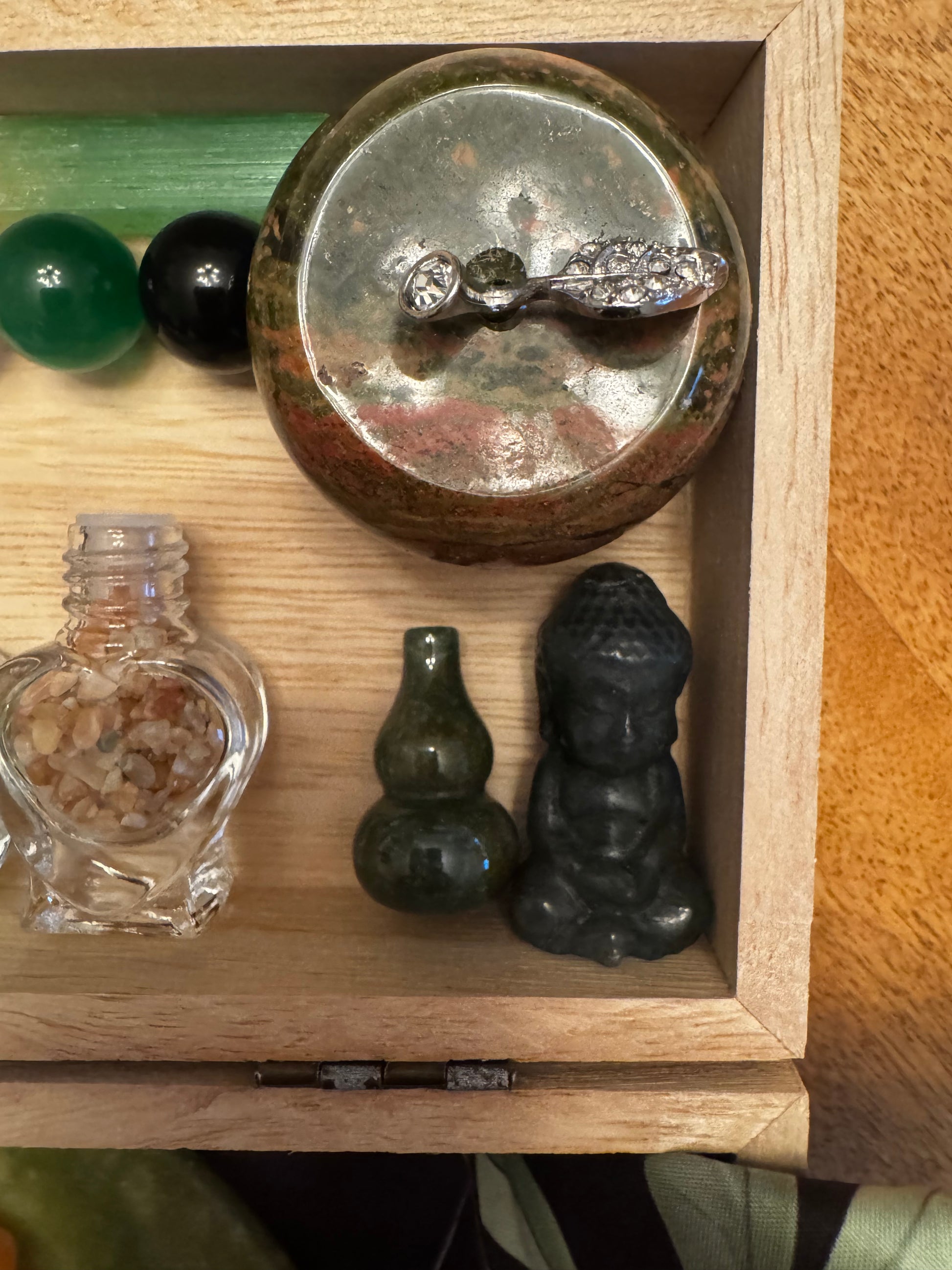 Wooden box with small crystals, glass heart bottle, and a tiny Buddha statue.