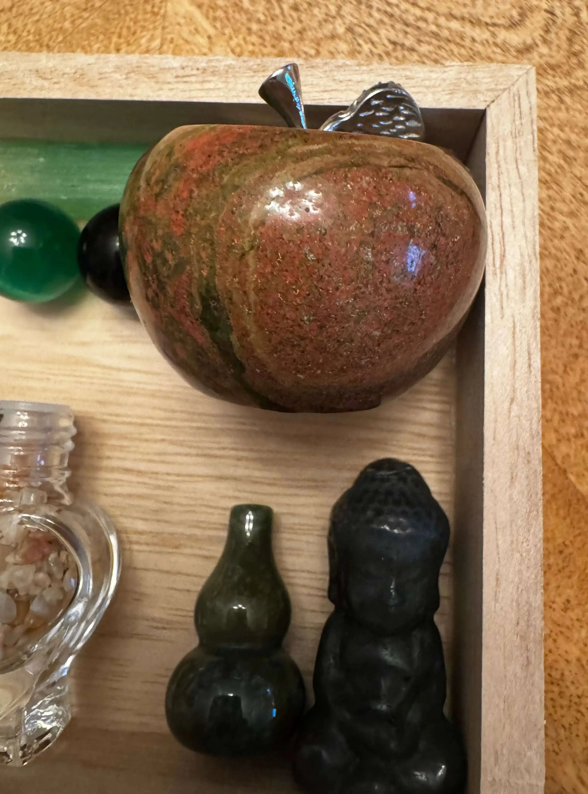 Wooden tray with stone objects including an apple, Buddha, and glass bottle.